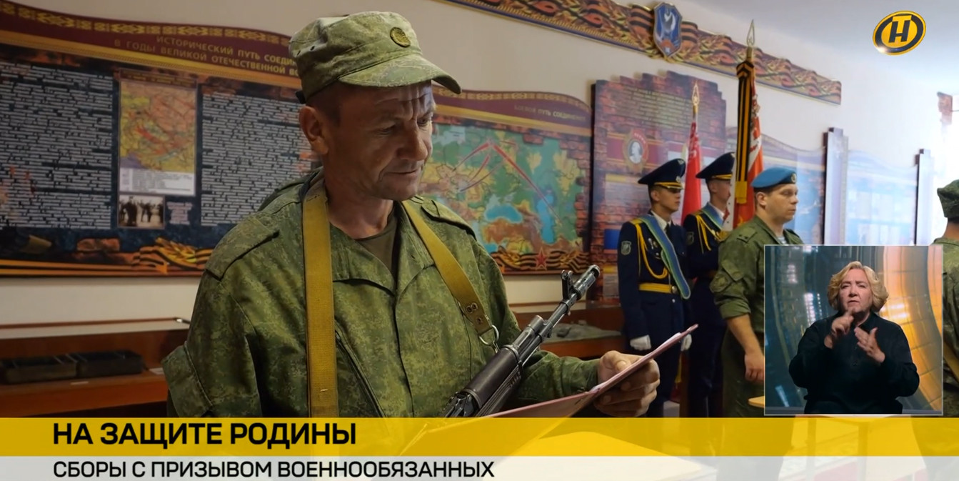 Новостной кадр ОНТ: военнообязанный принимает присягу с автоматом в руках. На заднем плане стоит почетный караул. Внизу плашка «На защите Родины».