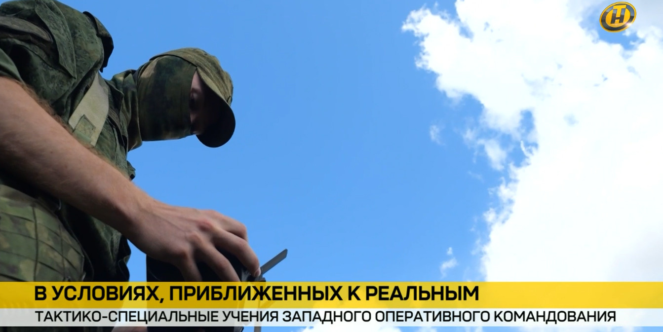 Военнослужащий в камуфляже и балаклаве настраивает оборудование на учениях Западного оперативного командования. Снимок снизу на фоне синего неба. Внизу плашка новостей ОНТ.